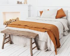 a bedroom with white walls and wood flooring, a bed covered in an orange blanket