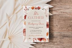 a wedding card on top of a wooden table with paper fans and flowers in the background