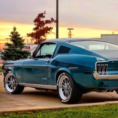 a blue mustang parked on the street in front of a parking lot at sunset or dawn