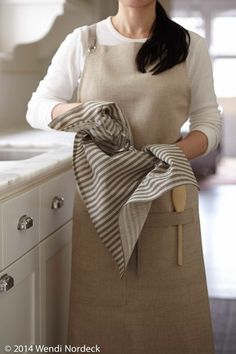 a woman standing in front of a kitchen counter holding a dish towel and wooden spoon