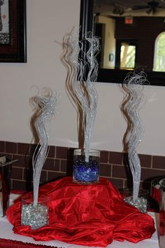 three glass vases with water in them sitting on a red table cloth next to a mirror