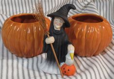 a statue of a witch holding a broom next to two pumpkins on a bed