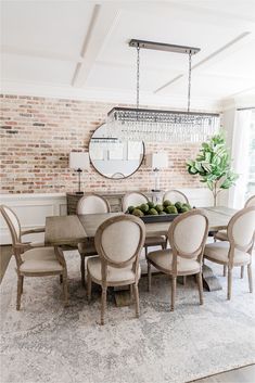 a dining room table with chairs and a mirror on the wall above it, in front of a brick wall