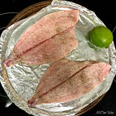 two fish fillets sitting on top of tin foil next to a lemon and lime