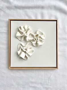 some white flowers are in a frame on a bed sheet and it looks like they have been made out of paper