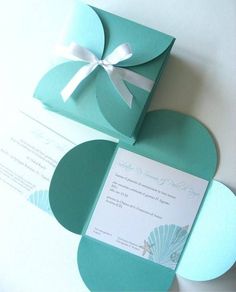 an open green box with a white ribbon on it and some cards in the shape of hearts