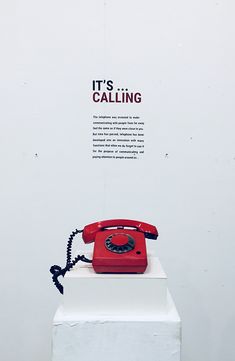 an old red telephone sitting on top of a white pedestal in front of a wall