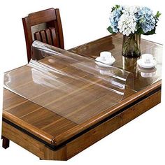 a wooden table topped with a glass top covered in a clear plastic cover next to a vase filled with white and blue flowers