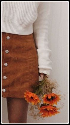 a woman holding flowers in her hand and wearing a white sweater with buttons on it