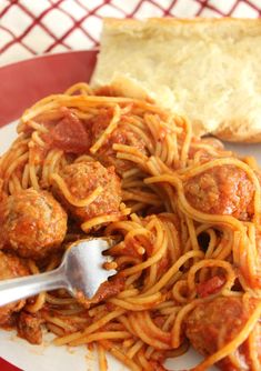 spaghetti with meatballs and bread on a red and white plate, ready to be eaten