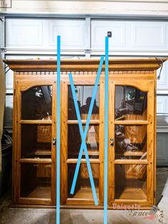 a wooden cabinet with glass doors and blue tape on the bottom shelf, in front of a garage door