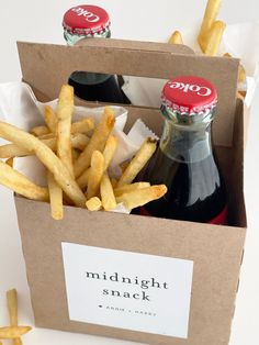 two bottles of soda and french fries in a cardboard box on a white table top