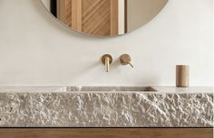 a bathroom sink with two faucets and a round mirror