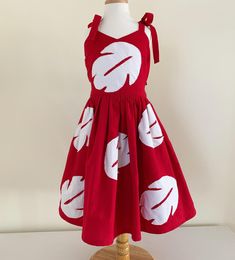 a red and white dress on a mannequin stand with a wooden dummy in the background