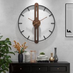 a large clock mounted to the side of a white wall next to a black dresser