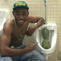 a man sitting on a urinal with a pineapple in it