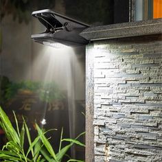 an outdoor light shines brightly on the side of a brick wall in front of some plants