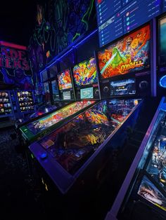 several pinball machines are lined up in a dark room with neon lights on them