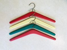 four different colored hangers are hanging on a white wall and one has a metal hook