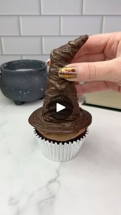 a hand holding a chocolate cupcake with a witch's hat on top