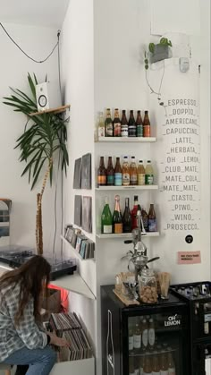 a woman sitting in front of a shelf filled with bottles