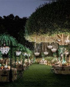 an outdoor dinner setup with chandeliers and greenery on the trees at night