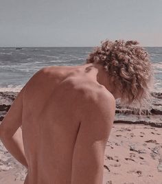 a naked man standing on top of a sandy beach next to the ocean with his back turned