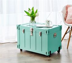 a table with a trunk on it sitting in front of a chair and a potted plant