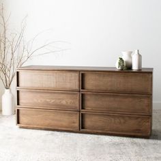 a wooden dresser sitting on top of a white carpeted floor next to vases