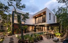 a modern house with an outdoor dining area and pool in the middle of it, surrounded by trees