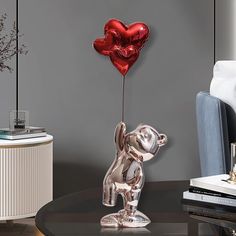 a metal bear holding a heart shaped balloon on top of a table in a living room