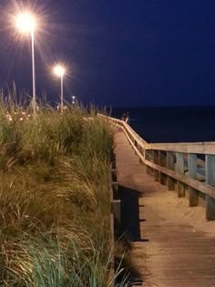 the boardwalk is lit up at night by street lights and grass on either side of it