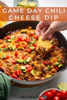 a hand dipping a tortilla chip into a skillet filled with game day chili cheese dip