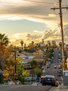 cars are parked on the street in front of some buildings and palm trees at sunset