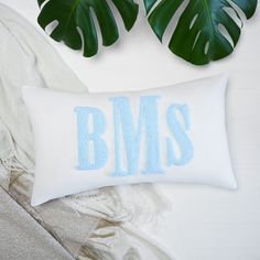 a white pillow with the word bms on it next to some plants and blankets