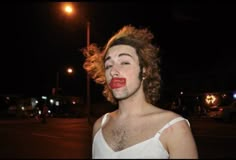 a man with his hair blowing in the wind and wearing a white shirt is standing outside at night