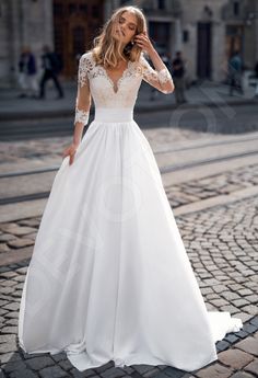 a woman in a white wedding dress standing on a cobblestone street with her hands to her face