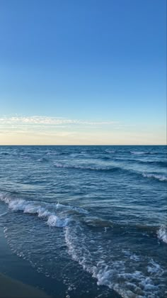 the ocean waves are rolling in and out on the beach, with blue skies above