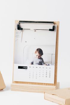 a desk calendar with a wooden block next to it on a white surface, and a photo of a baby