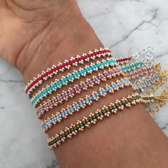 a woman's arm with several different colored bracelets on top of each other