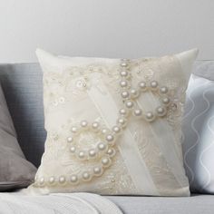 a white pillow with pearls on it sitting on a couch next to pillows and throw pillows