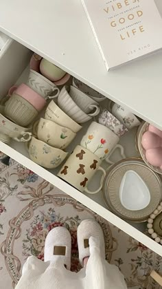 an open drawer with cups and saucers in it, next to a book on the table