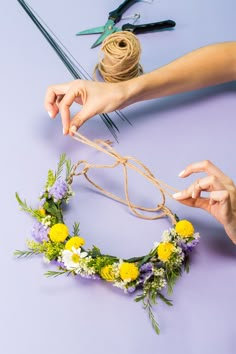 two hands are making a flower crown out of twine and flowers on the table