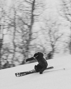 a man riding skis down the side of a snow covered slope with trees in the background