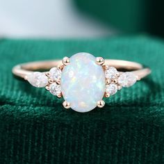 a white opal and diamond ring sitting on top of a green cloth