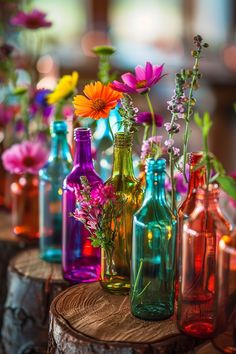 there are many different colored glass bottles on the tree stumps with flowers in them