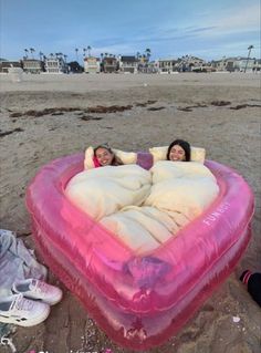 two people laying in an inflatable heart shaped bed on the beach