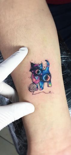 a cat tattoo on the left inner arm and wrist is shown in blue, pink, yellow and green colors