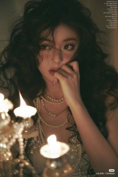 a woman is posing in front of candles and chandeliers with her hands on her face