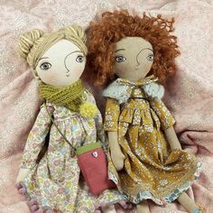 two dolls sitting on top of a bed next to each other